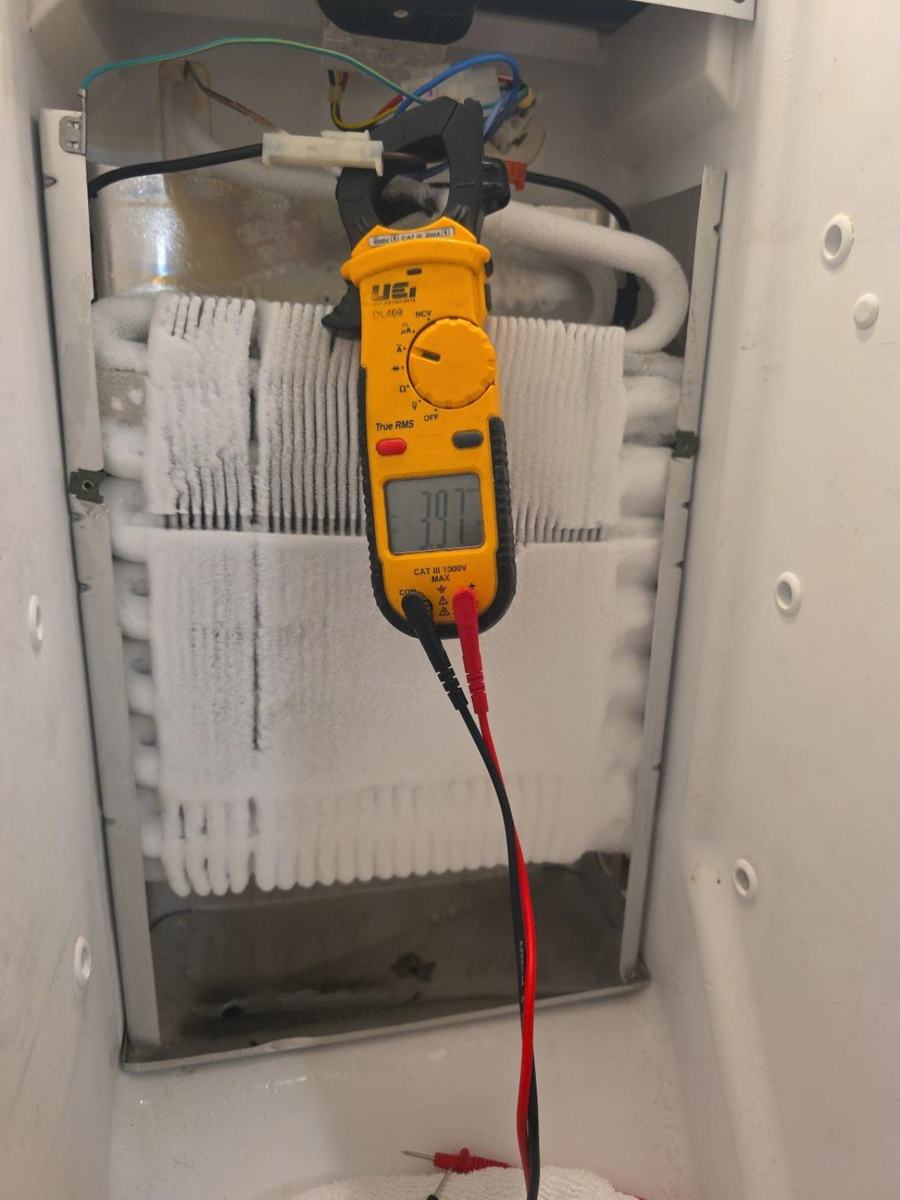 Clamp meter measuring defrost heater current on a Frigidaire refrigerator during service-mode testing